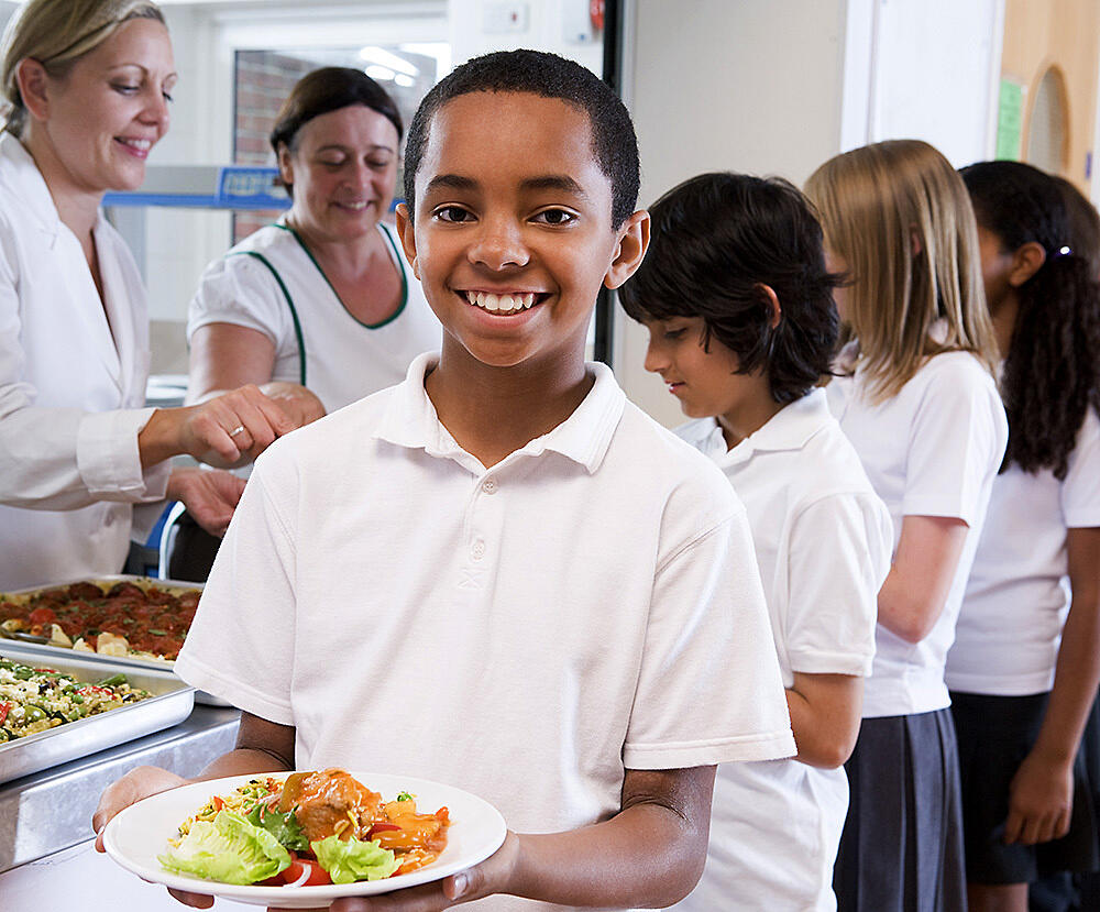 A boy holds a healthy meal in a cafeteria line.