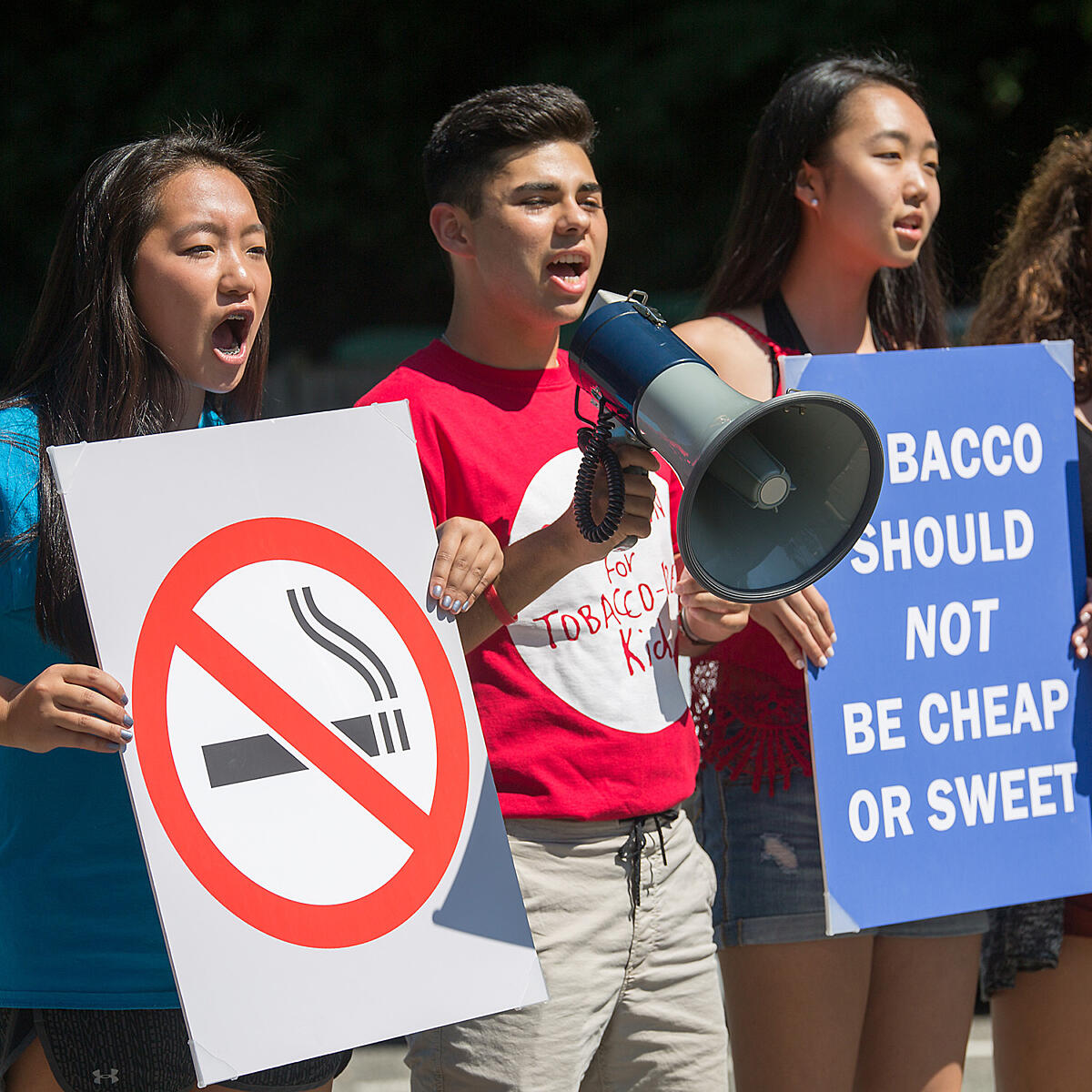 Youth hold signs and a megaphone while protesting tobacco.