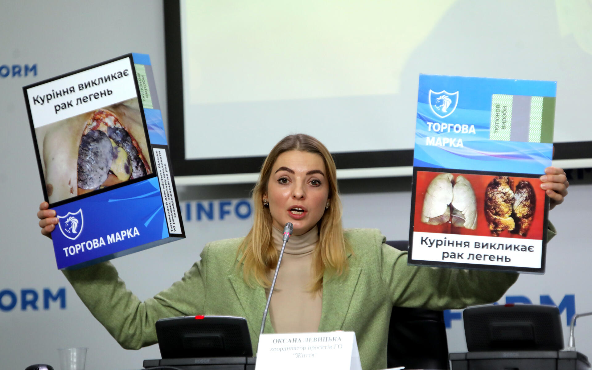 A woman holds up examples of Ukraine tobacco package warnings.